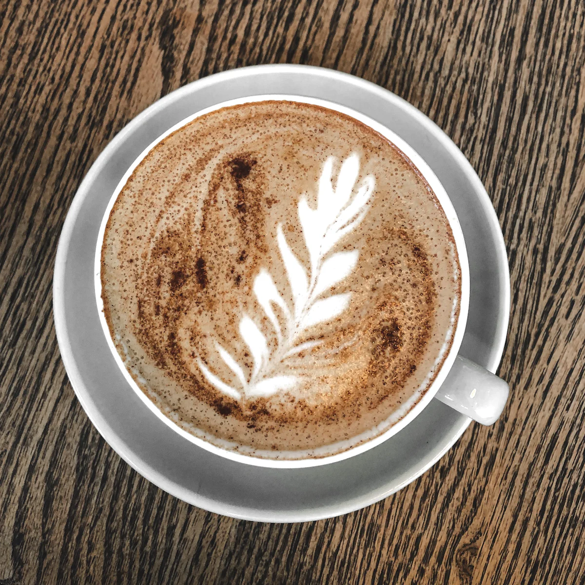 Taza de café con leche con arte latte, servida sobre una mesa de madera